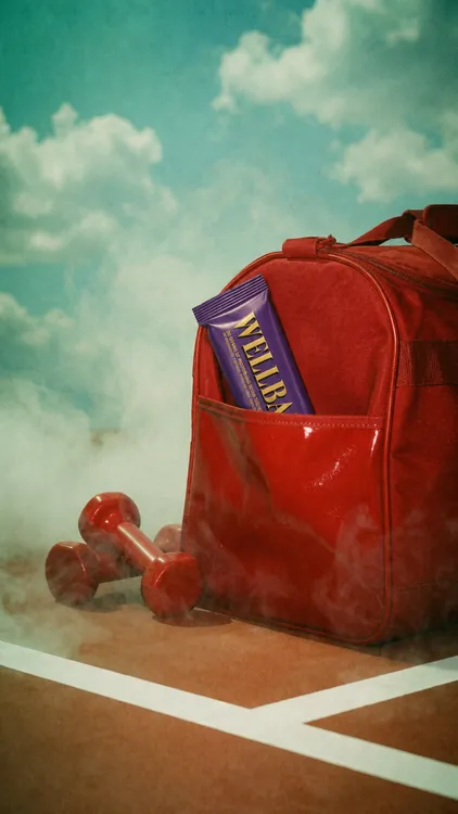 WELLBAR protein bar tucked in a red duffel bag amid clouds, brand campaign by Renuvo Design Inc.