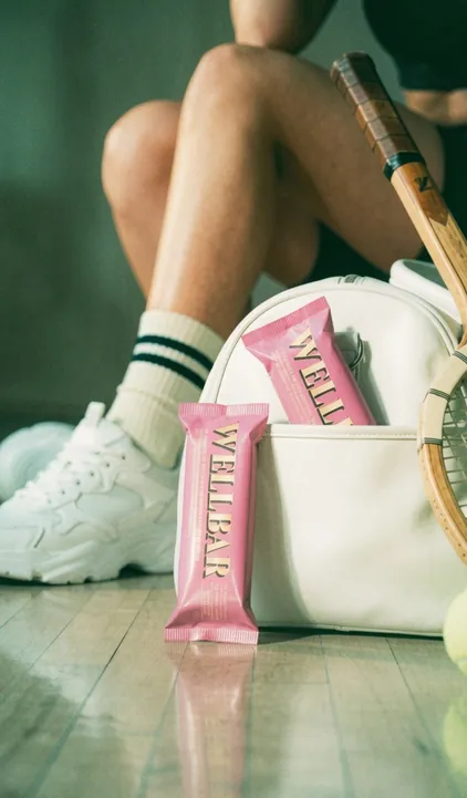 WELLBAR protein bar with a white gym bag and sneakers, brand campaign by Renuvo Design Inc.